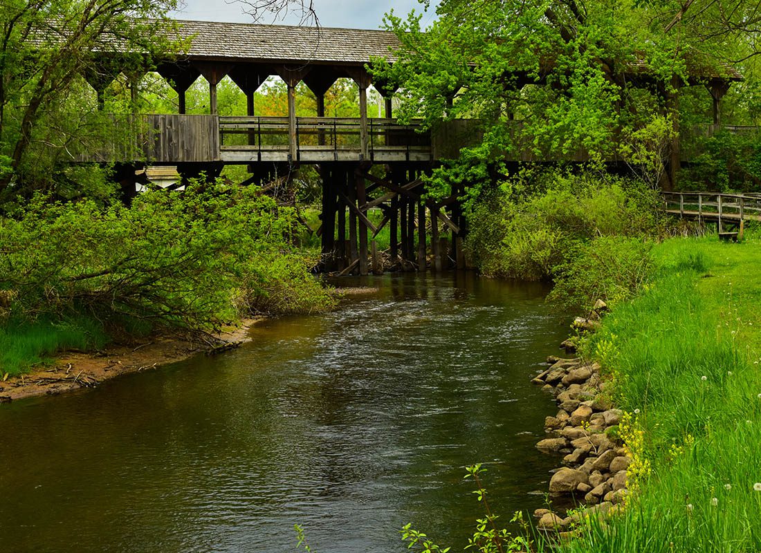 Grant, MI - Small River With a Wooden Covered Bridge Crossing it in a Green Forest