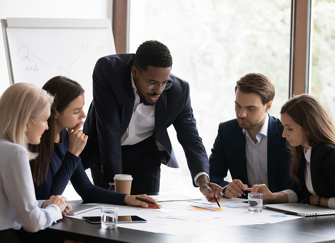 Insurance Solutions - Group of Business Professionals Looking at Documents a Speaker is Pointing at in an Office